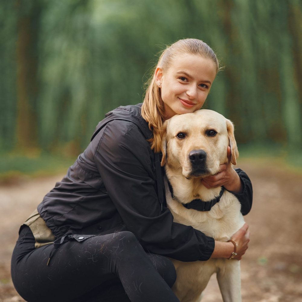 Owner and labrador retriever dog in a forest. Attractive sporty woman with dog. Golden retriever.